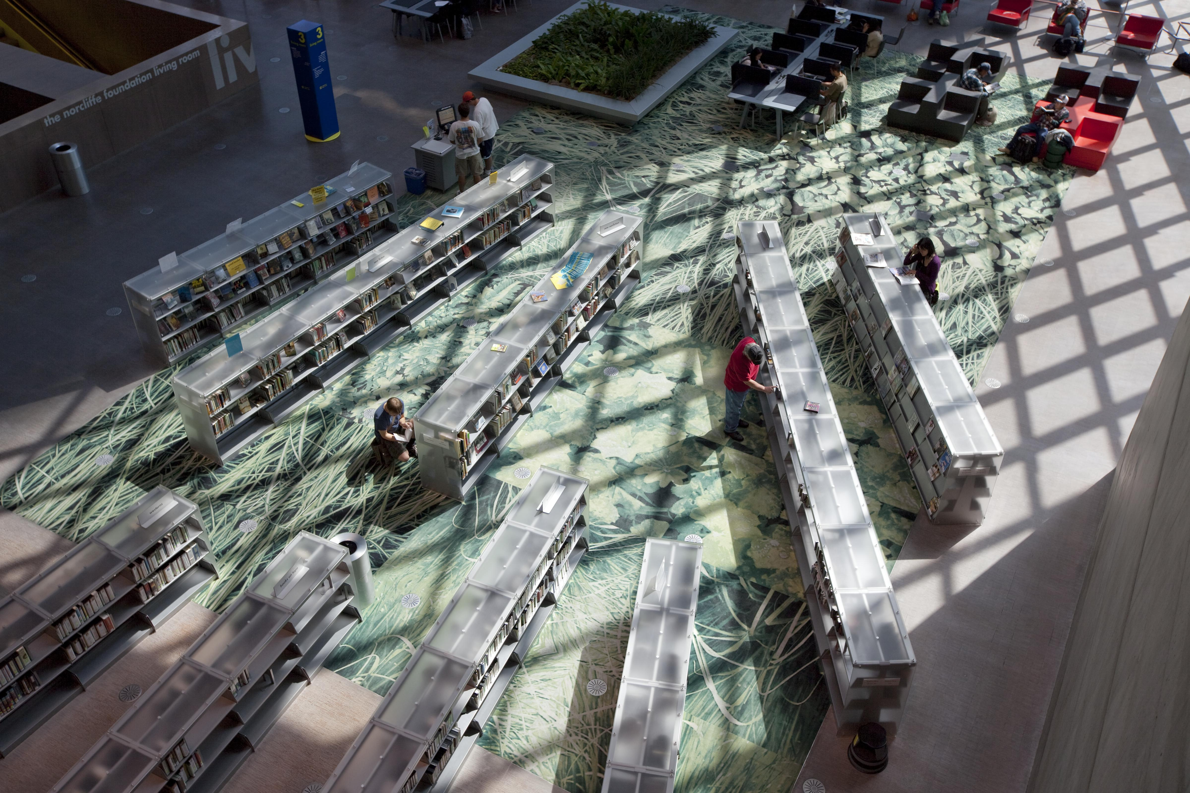 Sunlight falling across readers and rows of bookshelves on the open floor of the Seattle Central Library